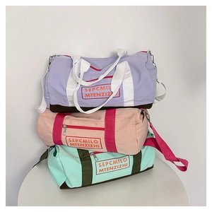 Drei bunte zylindrische Reisetaschen in Hellviolett, Rosa und Minzgrün auf einem Tisch