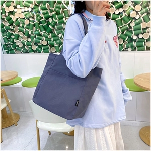 Detailed view of the canvas tote bag showing front pockets and fashion label detail
