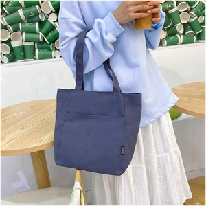 Close-up of deep blue canvas tote bag featuring front pocket and Fashion tag detail