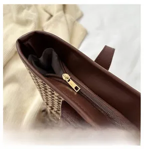Détail d'une fermeture éclair dorée sur un sac cabas en cuir marron et pied-de-poule