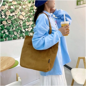 Close-up of brown canvas tote bag with fashion label against a creative green wall