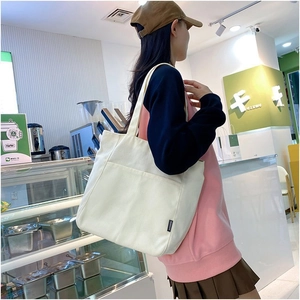 Detail shot of the cream canvas tote bag showing the front pocket and fashion label