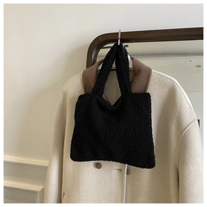 Detail of black faux shearling tote bag hanging against a white wool coat background