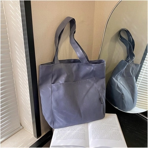 Detail of blue-grey canvas tote bag showing front pocket and black fashion label