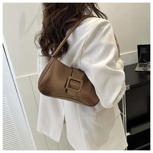 Detalle de un bolso baguette de color bronce metálico con una chaqueta blanca
