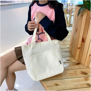 Minimalist beige canvas tote bag with front pocket shown in a lifestyle indoor setting