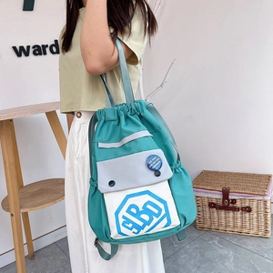 Side view of a mint green nylon drawstring backpack with contrast white pocket and badge