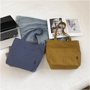 Detail of grey-blue and mustard yellow canvas tote bags with practical front pockets
