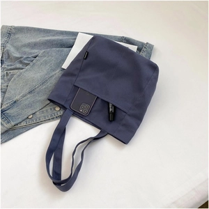 Detail of blue canvas tote bag with front pocket holding a smartphone and lipstick