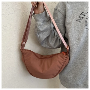 Detail view of brick red crescent crossbody bag with adjustable wide strap on model