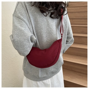 Close-up of a deep red crescent shoulder bag worn with an adjustable wide strap