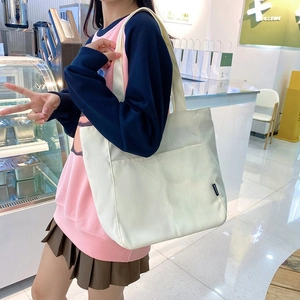 Minimalist off-white canvas tote bag for women featuring large front pocket and shoulder straps