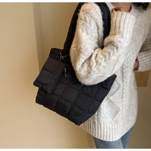 Detail of black quilted shoulder bag with hexagonal pattern and small hanging pouch