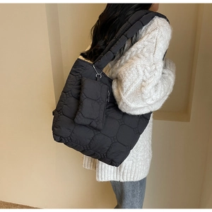 Detail view of black quilted tote bag and detachable pouch on female model in casual style