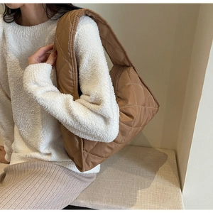 Detailed view of brown quilted shoulder bag worn with a white sweater and skirt