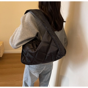 Detail view of large black quilted hobo bag worn by model in a minimalist setting