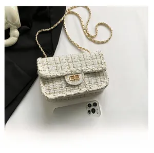 Detailed view of tweed crossbody bag with gold chain strap and metal lock next to a phone