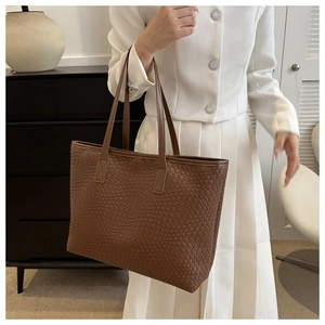 Braune geflochtene Leder-Einkaufstasche, präsentiert von einem Model im weißen Outfit