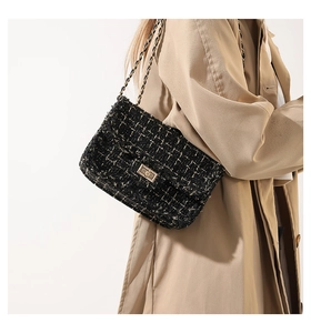 Close-up of black and gold tweed shoulder bag with metal chain strap on model