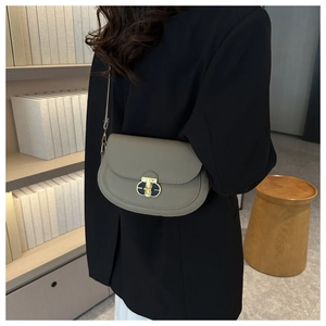 Detail view of a sage green textured leather saddle bag with a gold buckle worn by a model