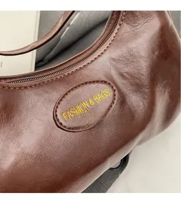 Detail of dark brown glossy leather handbag with embossed logo and metal zipper