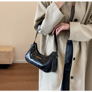 Detail of glossy black leather shoulder bag featuring a metallic fashion brand tag