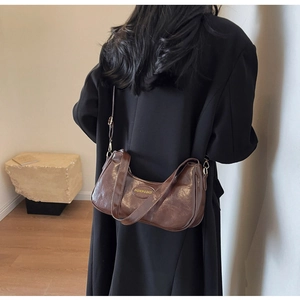 Detailed back view of a brown vintage crescent bag on a model wearing a black trench coat