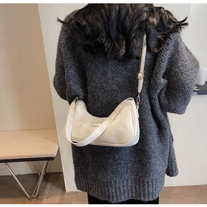 Close-up of a white pleated crescent moon crossbody bag with adjustable strap and metal logo