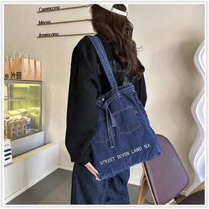 Detail of blue denim tote bag featuring white letter embroidery and bow decoration
