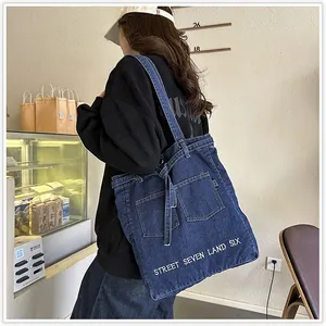 Detailed embroidery on a large blue denim tote bag worn by a model in a cafe setting