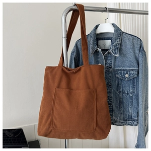 Detail of a brown corduroy tote bag with large front pocket hanging on a metal rack