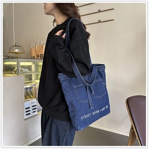 Detailed view of dark blue denim tote bag with white street style embroidery and pockets