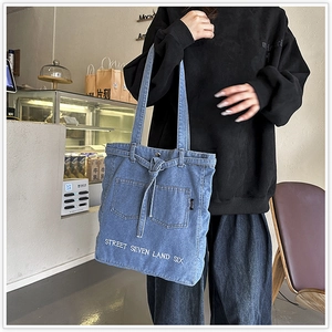Detail of blue denim tote bag with white embroidery and pockets in a casual cafe setting