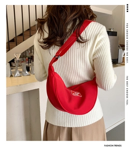 Detailed view of red crescent crossbody bag with white embroidery and wide strap