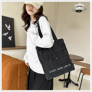 Detail of black denim tote bag showing large front pockets and Street Seven Land Six text