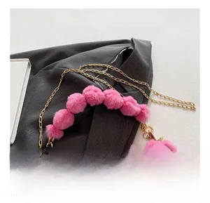 Detail of pink faux fur handbag showing gold chain strap and fluffy pom-pom handle