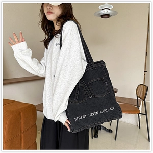 Detail of black denim tote bag with street style embroidery and deconstructed pocket