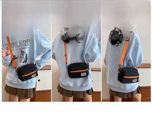 Detail view of the black canvas crossbody bag with orange accents and adjustable strap