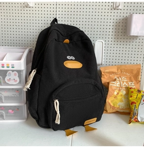 Close-up of black corduroy duck backpack with yellow bill and leather fashion label