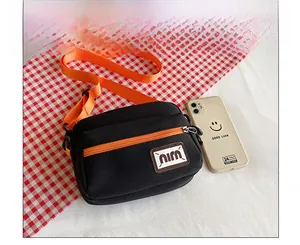 Detail of black canvas crossbody bag featuring vibrant orange adjustable strap and nina logo