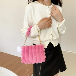 Close-up of pink faux fur shoulder bag featuring golden chain strap and white pompom detail