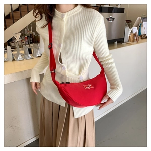 Detail of red crescent canvas crossbody bag featuring adjustable nylon strap and woven label