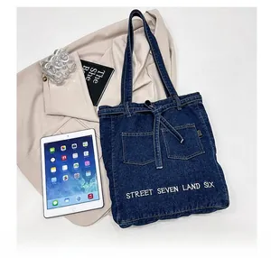 Detailed close-up of dark blue denim tote bag with white street seven embroidery text