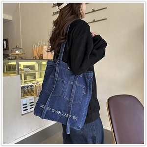 Detail of a navy denim tote bag with pocket design and street-style text in a cafe setting