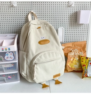 Detail view of a cream-colored corduroy student backpack featuring a cute cartoon duck design