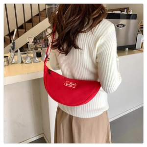 Close-up of a red crescent-shaped canvas crossbody bag with YUN QING logo worn by a model