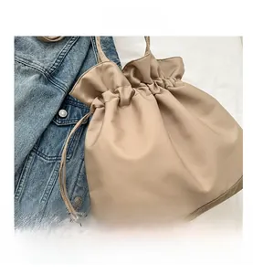 Close-up of khaki drawstring bucket bag with leather texture beside denim jacket