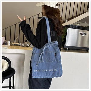 Detail view of denim tote bag with white embroidery and functional front pockets