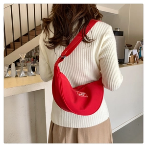Detail of red crescent hobo bag featuring white logo patch and adjustable wide strap
