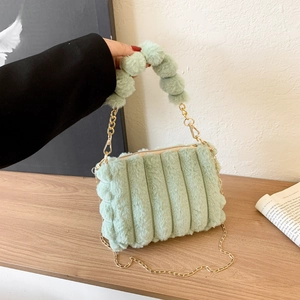 Detail of mint green plush handbag featuring vertical quilting and golden chain strap